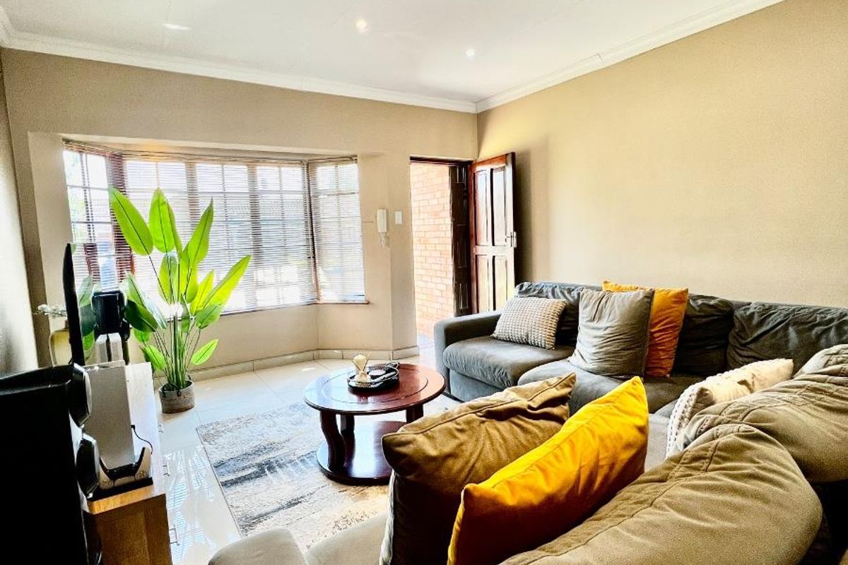 A comfortable living room featuring a large bay window, tiled flooring, and recessed downlighting, creating a bright and inviting space.