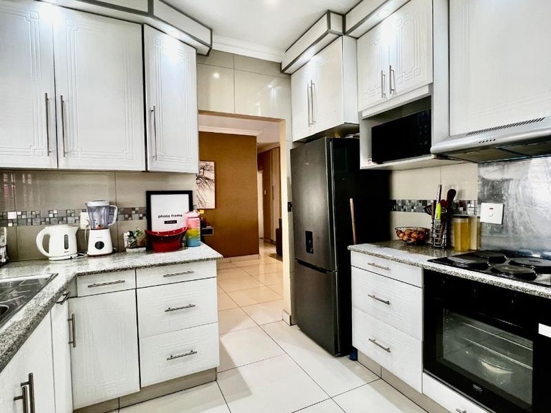 Modern kitchen featuring white cabinetry, granite countertops, built-in oven, hob, extractor fan, and tiled flooring with a mosaic backsplash.