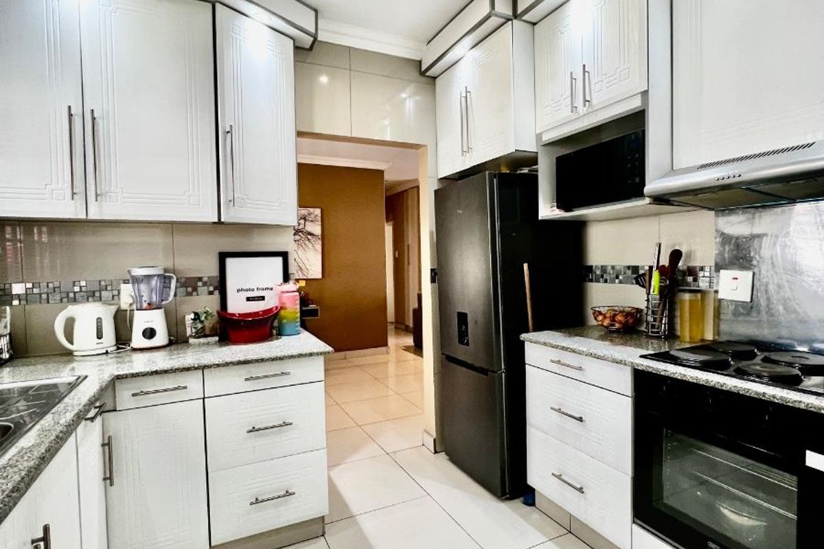 Modern kitchen featuring white cabinetry, granite countertops, built-in oven, hob, extractor fan, and tiled flooring with a mosaic backsplash.