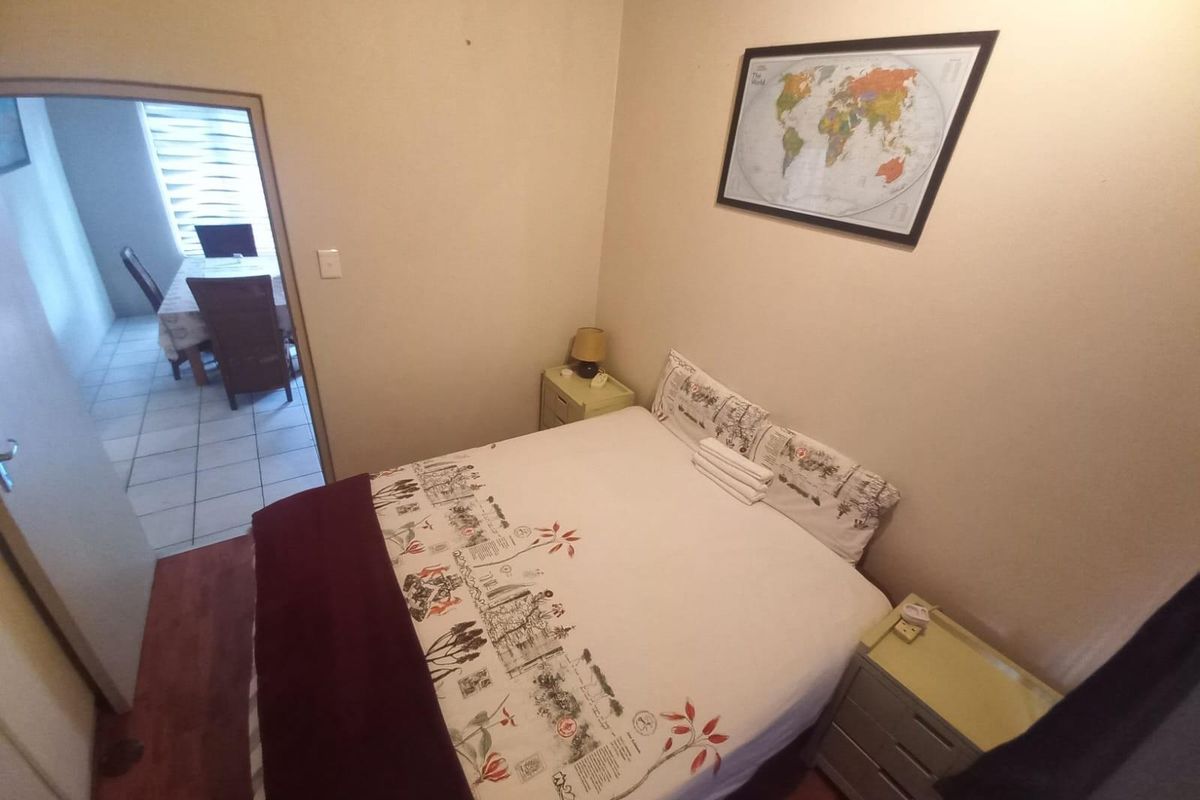 A compact bedroom featuring laminate flooring and neutral wall finishes, with a view into the adjacent dining area.