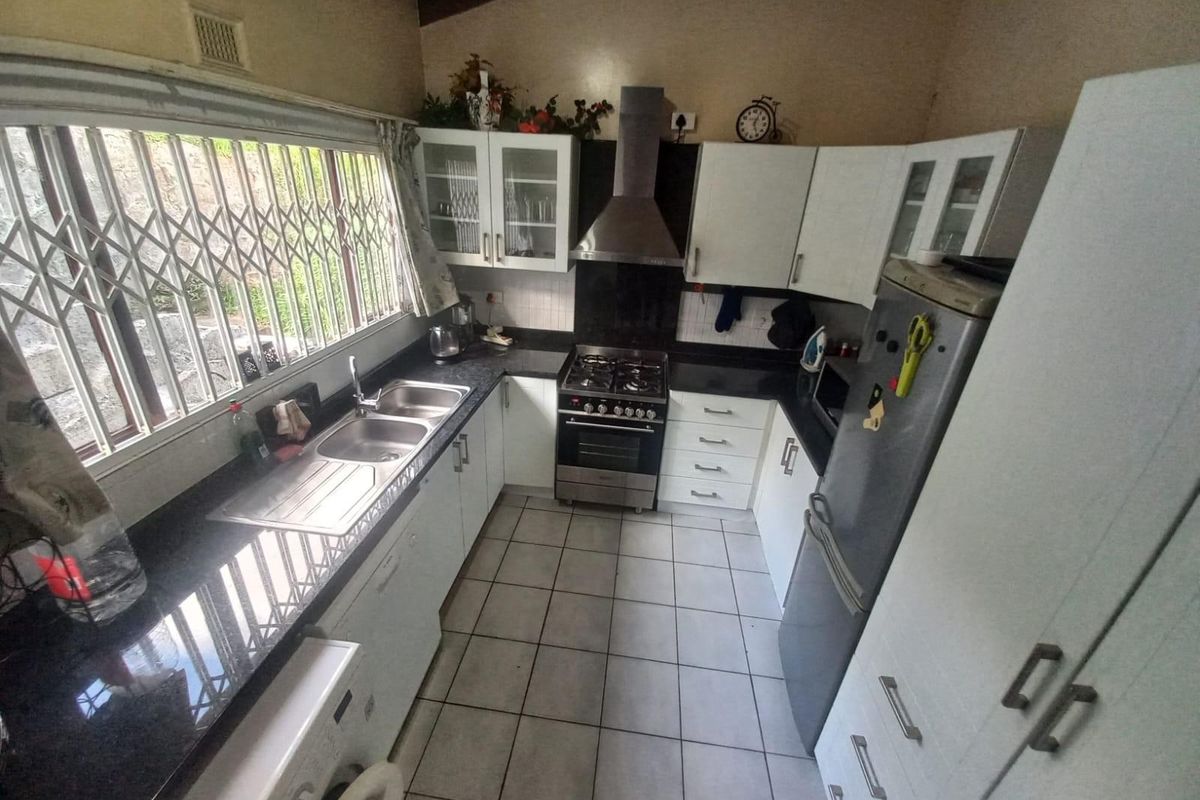 Functional kitchen featuring dark granite countertops, white cabinetry, gas stove with extractor fan, and tiled flooring with security bars on the window.