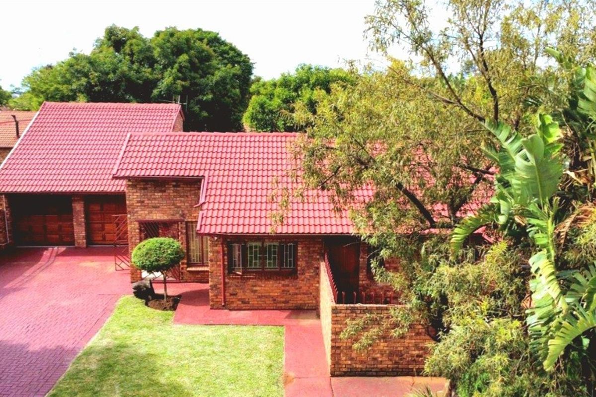 An elevated view of a brick-faced house featuring a red tiled roof, a paved driveway, and a double garage.