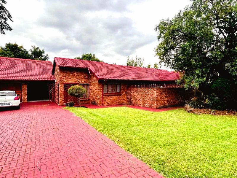 A well-maintained face-brick house featuring a red tiled roof, paved driveway, and a spacious front lawn.