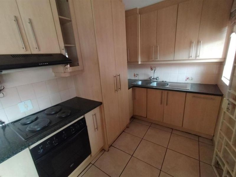 A functional kitchen featuring light wood cabinetry, dark countertops, a built-in oven, electric hob, extractor fan, and a double-basin sink with tiled flooring.