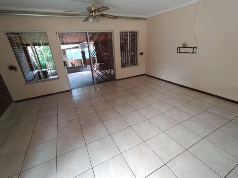 Spacious living area featuring neutral floor tiles, a ceiling fan, and sliding glass doors providing direct access to the outdoor patio.