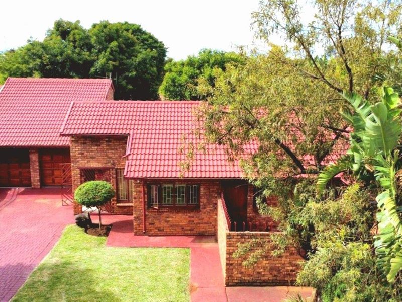 An elevated view of a brick-faced house featuring a red tiled roof, a paved driveway, and a double garage.