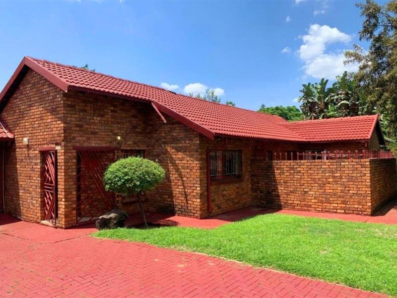 A single-story face-brick house featuring a red tiled roof, paved driveway, and a private enclosed garden area.