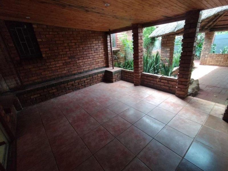 A covered patio area featuring exposed brick walls, a timber-clad ceiling, and tiled flooring, overlooking a garden space.