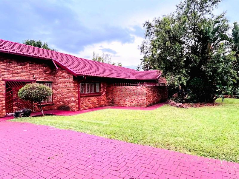 A single-story face-brick house featuring a tiled roof, paved driveway, and a well-maintained front lawn with mature garden landscaping.