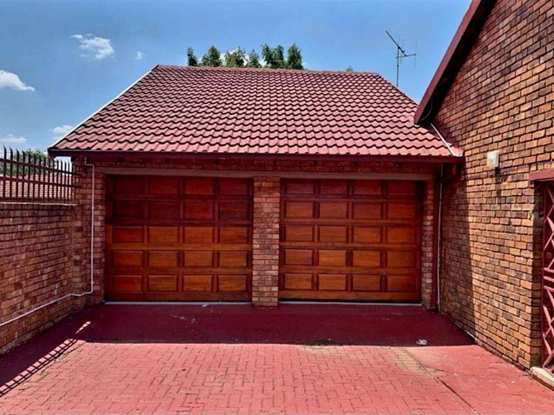 A double garage with wooden sectional doors, brick exterior walls, and a tiled roof, featuring a paved driveway area.