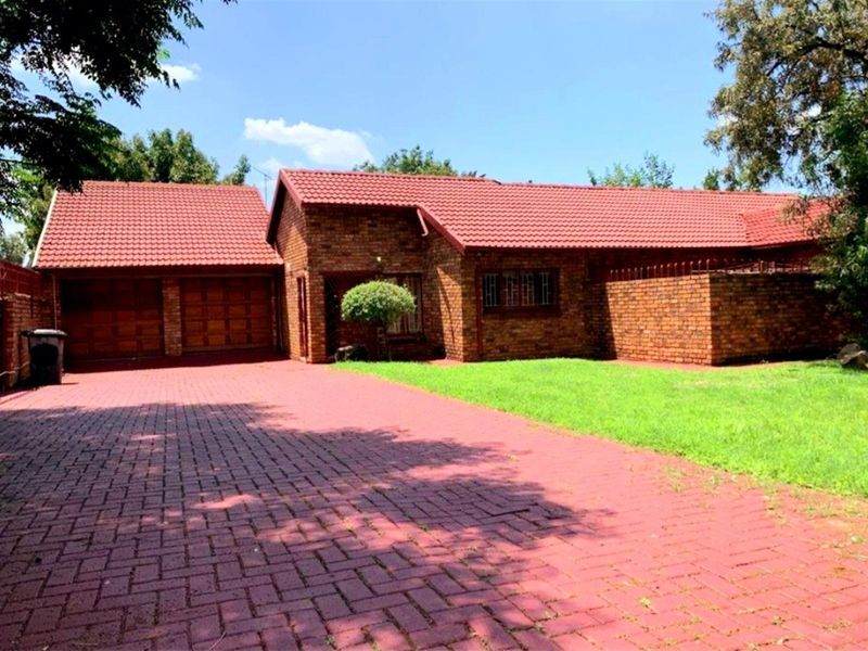 A well-maintained face-brick house featuring a tiled roof, double garage, and a paved driveway set within a neat garden.