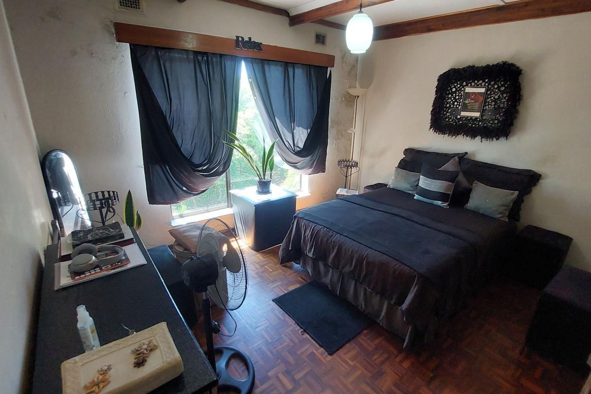 A bedroom featuring parquet timber flooring, exposed timber ceiling beams, and a large window with natural light.