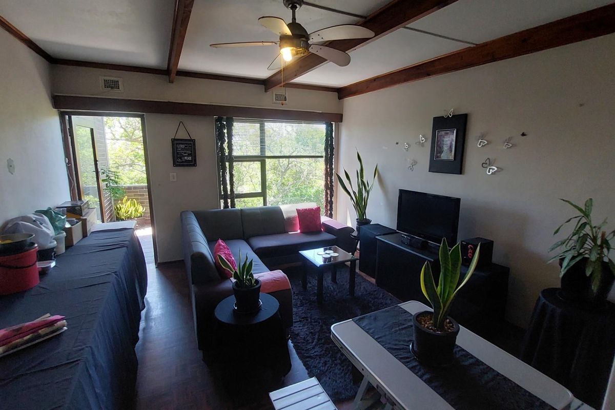 A living room featuring exposed timber ceiling beams, a ceiling fan, and direct access to an outdoor balcony area.