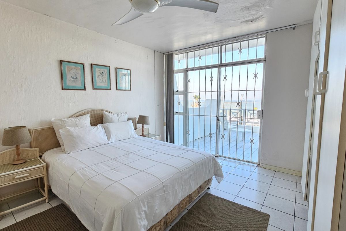Bright bedroom featuring tiled flooring, a ceiling fan, and a sliding glass door with security gate leading to an outdoor balcony area.