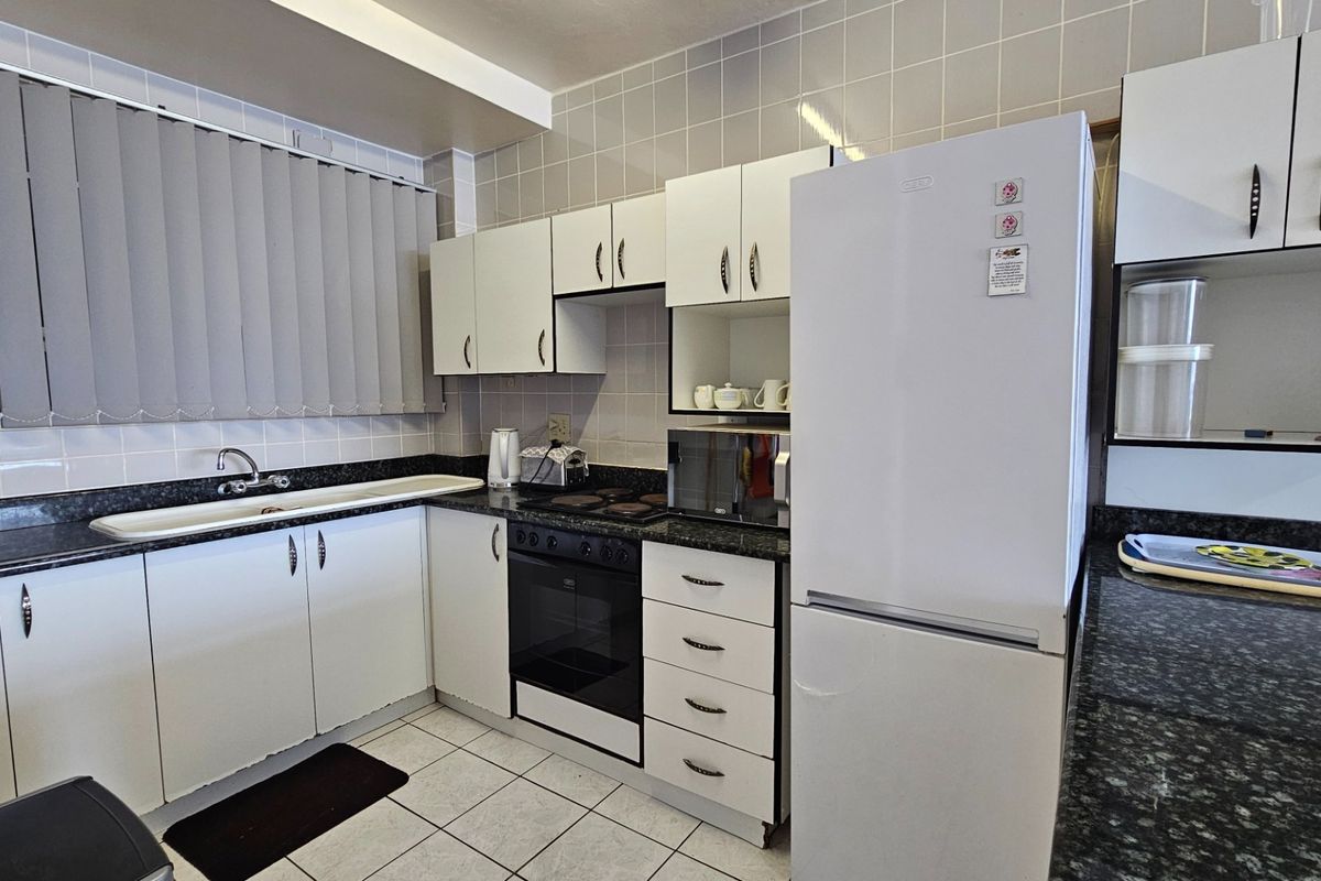 A functional kitchen featuring white cabinetry, dark laminate countertops, tiled backsplash, and built-in oven with electric hob.
