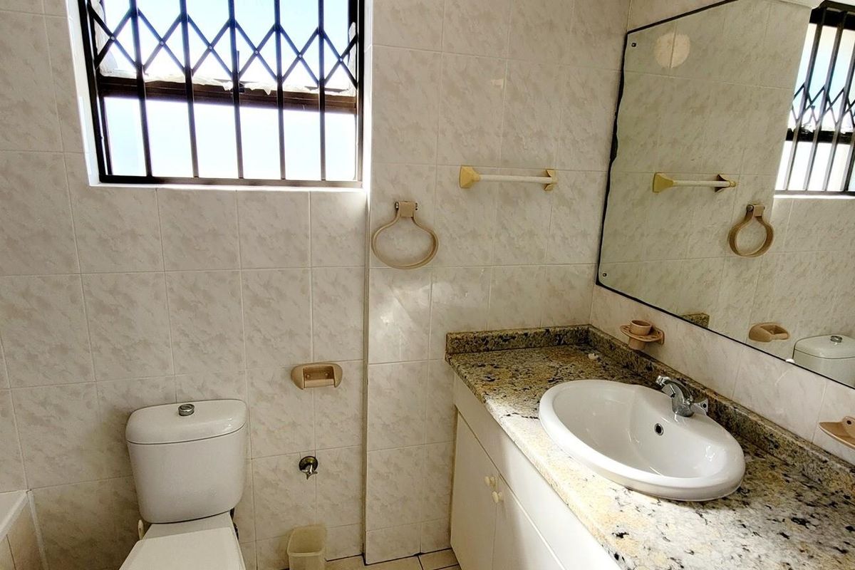 A functional bathroom featuring a granite vanity top, integrated basin, toilet, and a bathtub with wall-mounted shower fixtures.