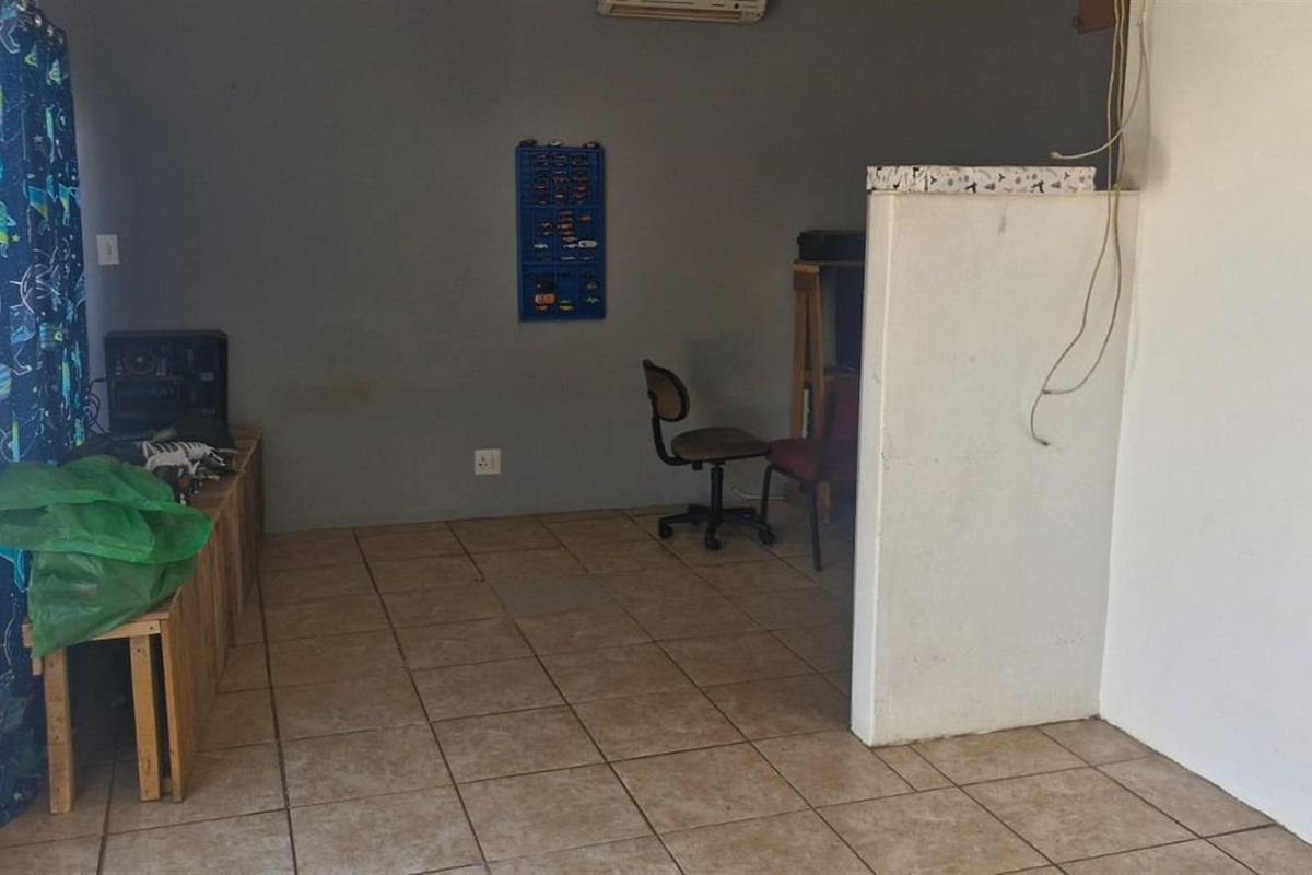 A multi-purpose living area featuring tiled flooring, a partition wall, and an installed air conditioning unit, requiring some cosmetic updates.