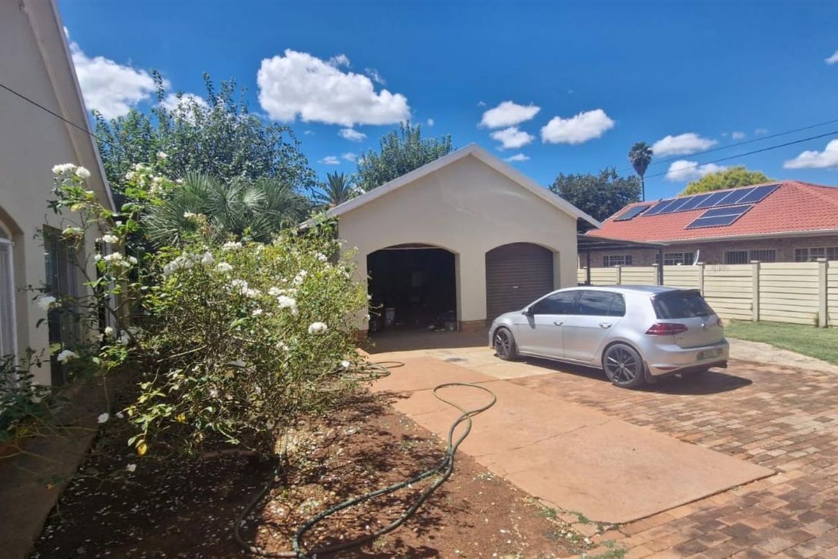 Rear exterior view featuring a double garage, paved driveway, and boundary wall, with solar panels visible on the adjacent roof structure.