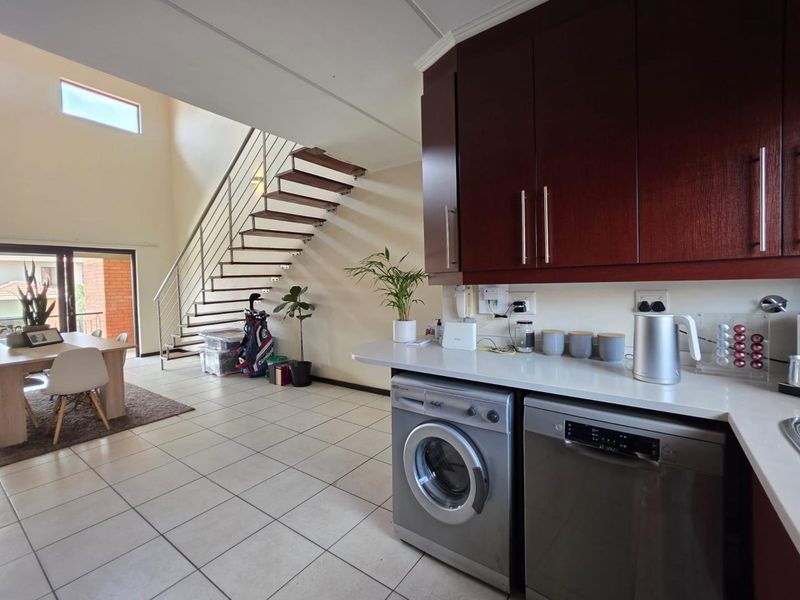 Open-plan kitchen and living area featuring dark wood cabinetry, stone countertops, tiled flooring, and a modern floating staircase leading to the upper level.