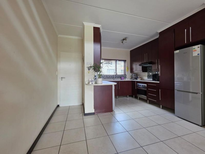 A functional kitchen featuring dark wood cabinetry, tiled flooring, a built-in oven with extractor fan, and a breakfast counter.