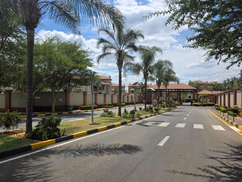 A view of the secure estate entrance road featuring paved driveway, landscaped verges, and perimeter walling.