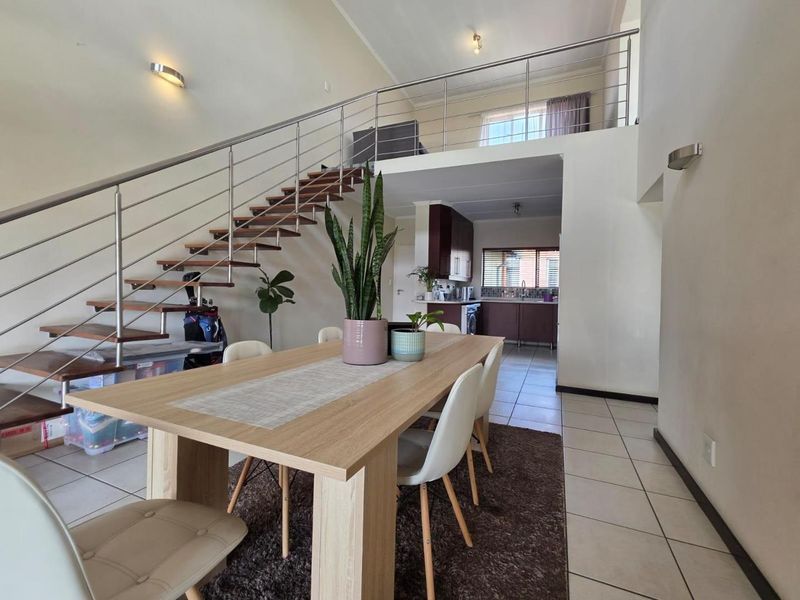 Open-plan living and dining area featuring a staircase with stainless steel balustrades leading to a mezzanine level, with an adjacent kitchen.