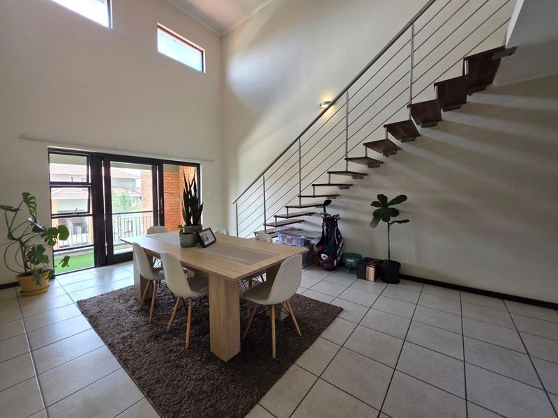 Spacious open-plan dining area featuring high ceilings, tiled flooring, and a modern floating staircase with stainless steel balustrades leading to the upper level.