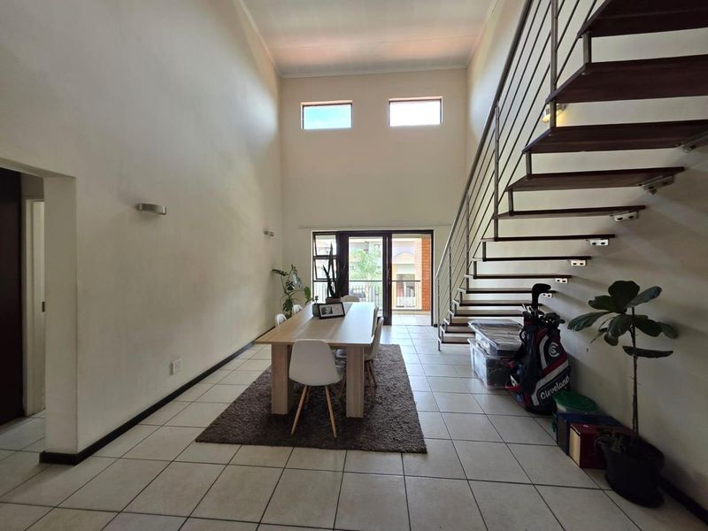 Spacious open-plan living area featuring high ceilings, tiled flooring, and a modern floating staircase leading to the upper level with access to a balcony.
