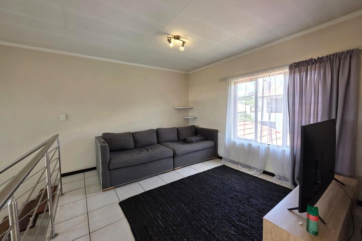 A living room area featuring tiled flooring, a stainless steel staircase railing, and a large window providing natural light.