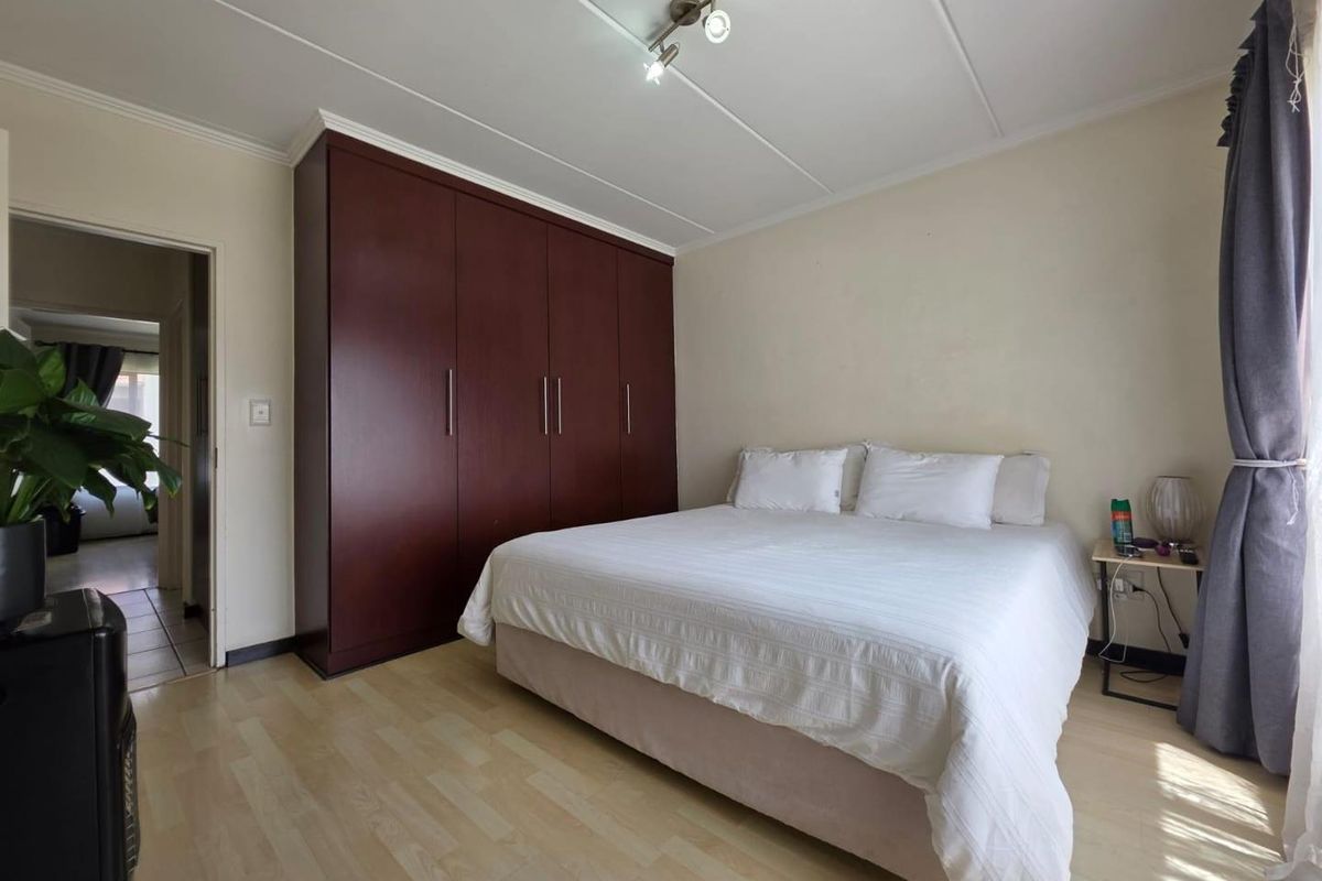 A bedroom featuring light-toned laminate flooring and a large, dark wood built-in wardrobe with ample storage space.