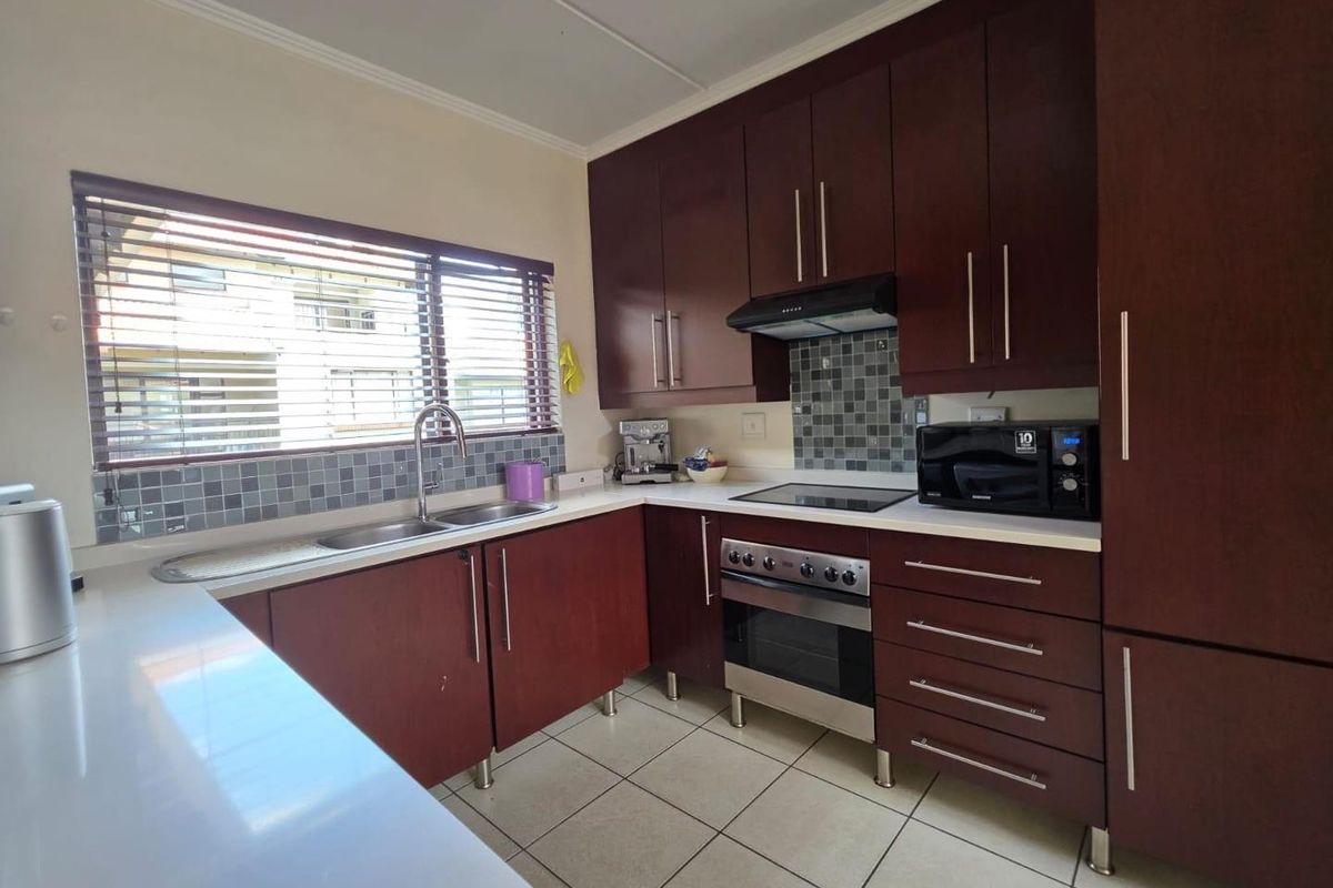 A functional kitchen featuring dark wood cabinetry, stone countertops, a mosaic tile backsplash, and built-in stainless steel oven and extractor fan.