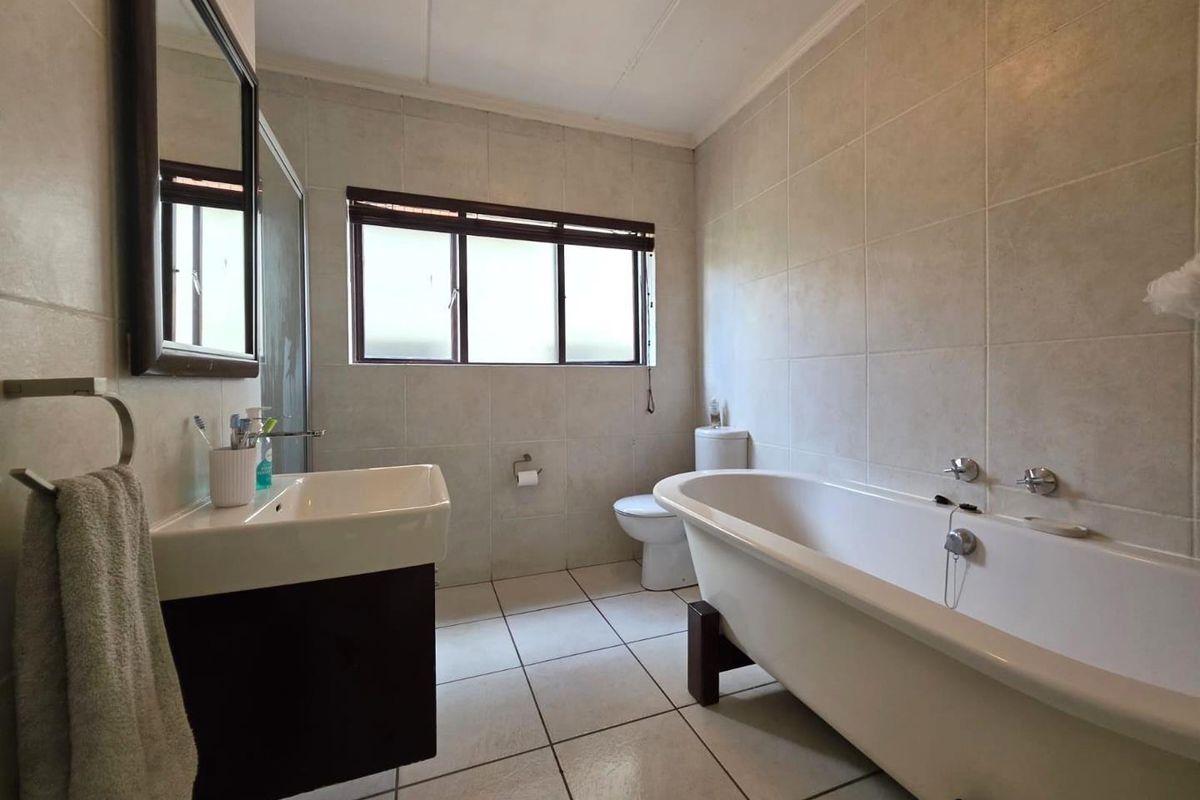 A well-maintained bathroom featuring a freestanding bathtub, a modern vanity with a basin, a toilet, and neutral wall and floor tiling.