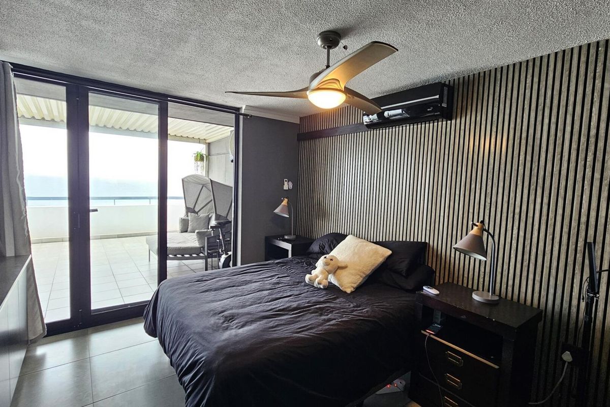 Modern bedroom featuring a stylish slatted timber accent wall, ceiling fan, split system air conditioning, and direct access to a private balcony.