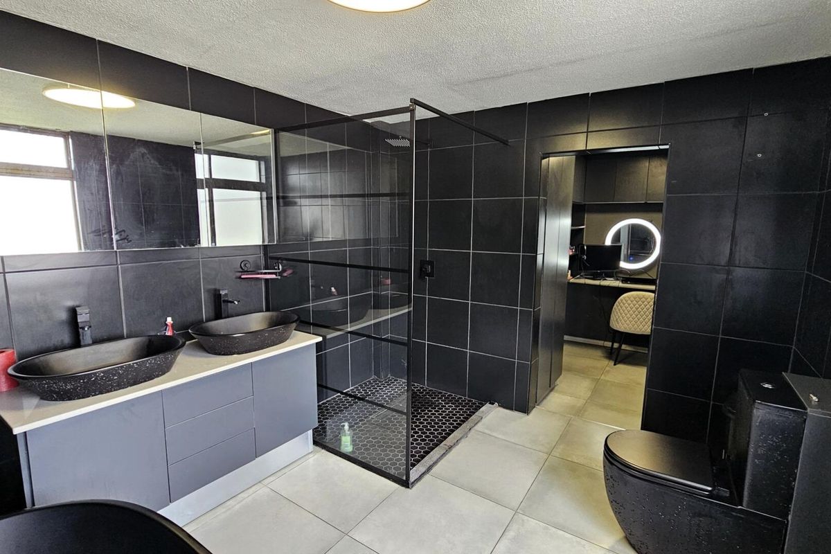 Modern bathroom featuring a double vanity with vessel sinks, a walk-in shower with black frame, and dark tiled walls.