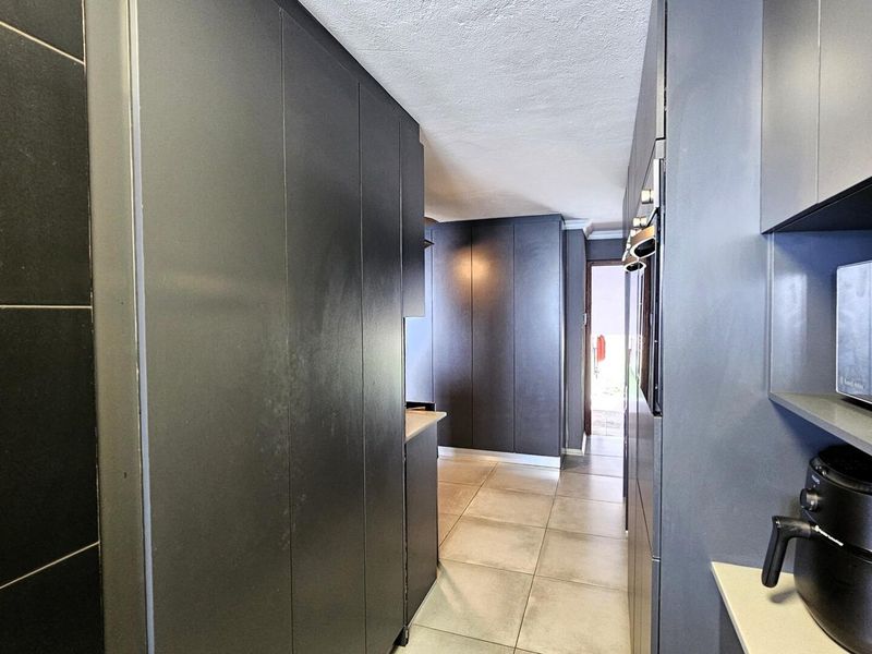 A modern galley-style kitchen featuring sleek dark cabinetry, integrated appliances, and neutral floor tiles, offering a clean and contemporary aesthetic.