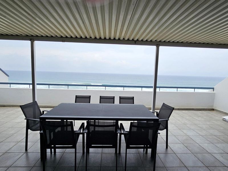 Spacious covered balcony featuring tiled flooring, a protective metal balustrade, and expansive, unobstructed ocean views.