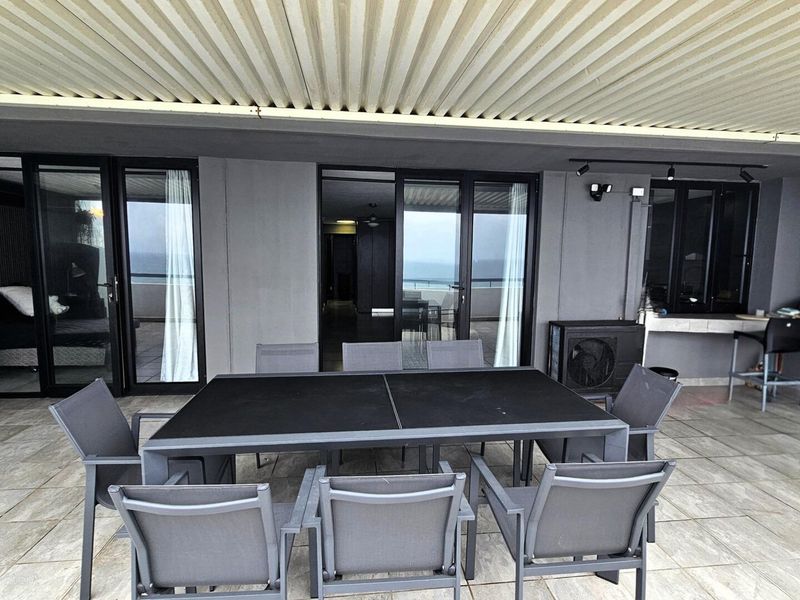 Spacious covered patio featuring tiled flooring, built-in fireplace, stone counter, and multiple sliding glass door access points to the interior living areas.