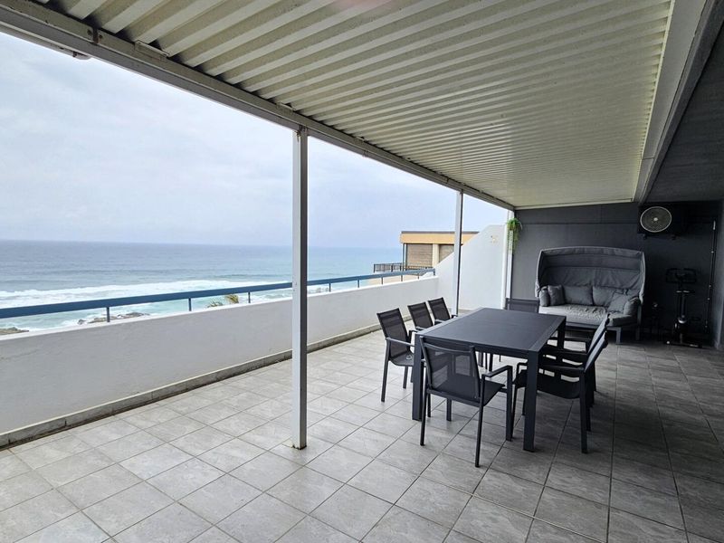 Spacious covered balcony featuring tiled flooring, metal railing, and expansive ocean views, providing an ideal outdoor entertainment area.