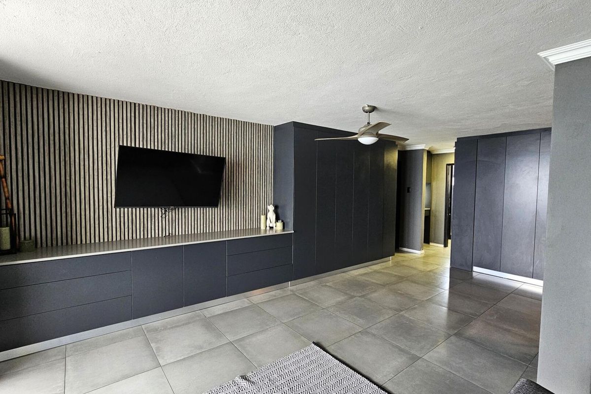 Modern living area featuring sleek dark built-in cabinetry, a stylish slatted wood feature wall, ceiling fan, and large format floor tiles.