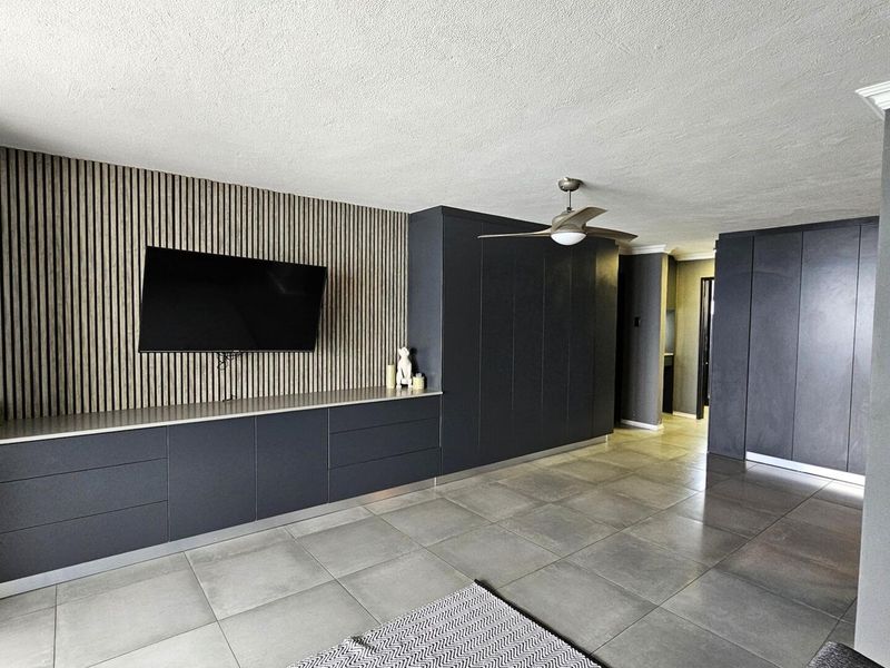 Modern living area featuring sleek dark built-in cabinetry, a stylish slatted wood feature wall, ceiling fan, and large format floor tiles.