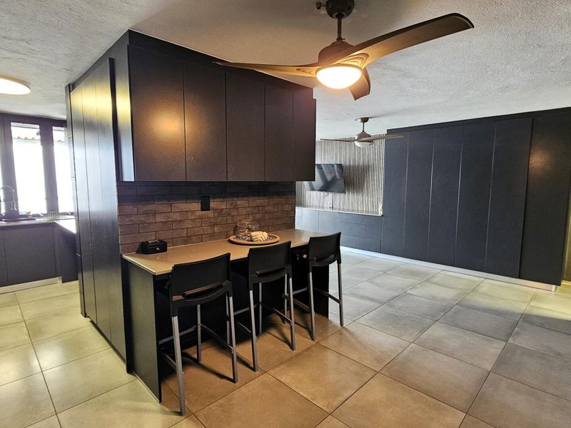 Modern open-plan living area featuring sleek dark cabinetry, a stone breakfast bar, tiled flooring, and contemporary ceiling fans.