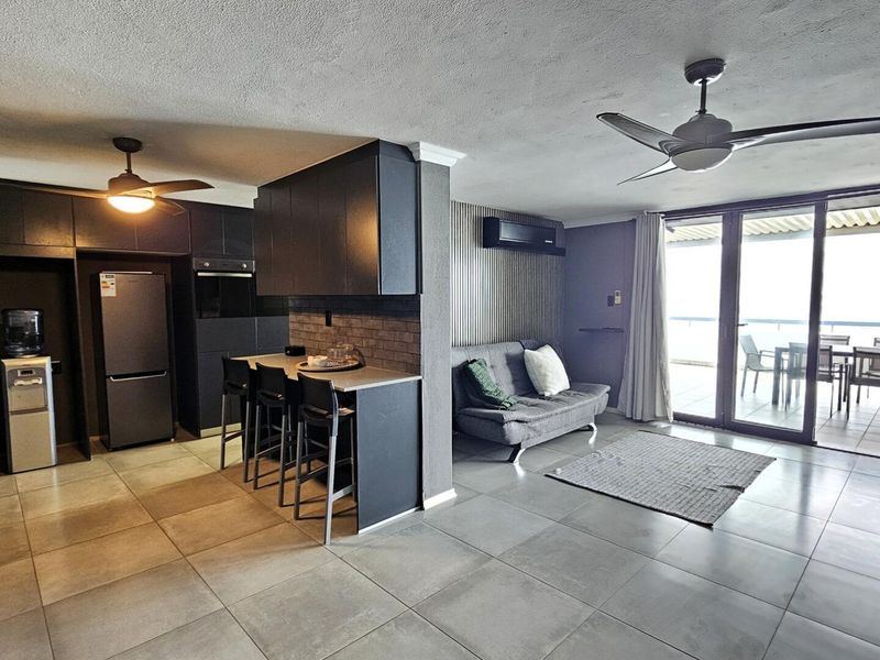 Modern open-plan living area featuring a sleek kitchen with breakfast bar, tiled flooring, ceiling fans, and direct access to a spacious balcony.