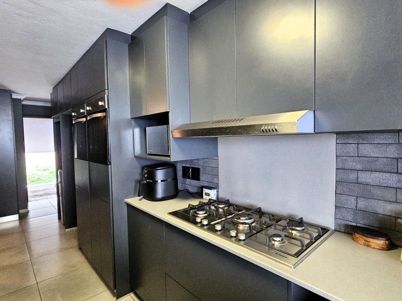Modern kitchen featuring sleek dark cabinetry, stone countertops, a gas hob with extractor fan, and integrated built-in ovens.