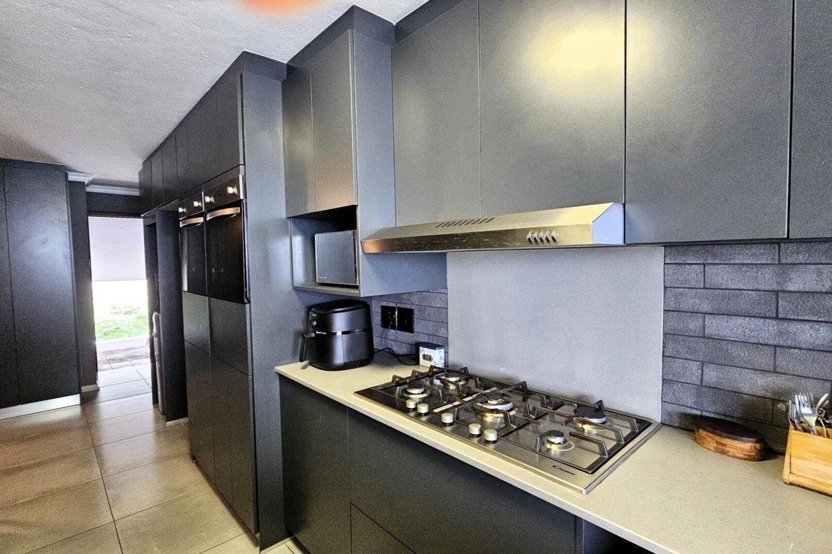 Modern kitchen featuring sleek dark cabinetry, stone countertops, a gas hob with extractor fan, and integrated built-in ovens.