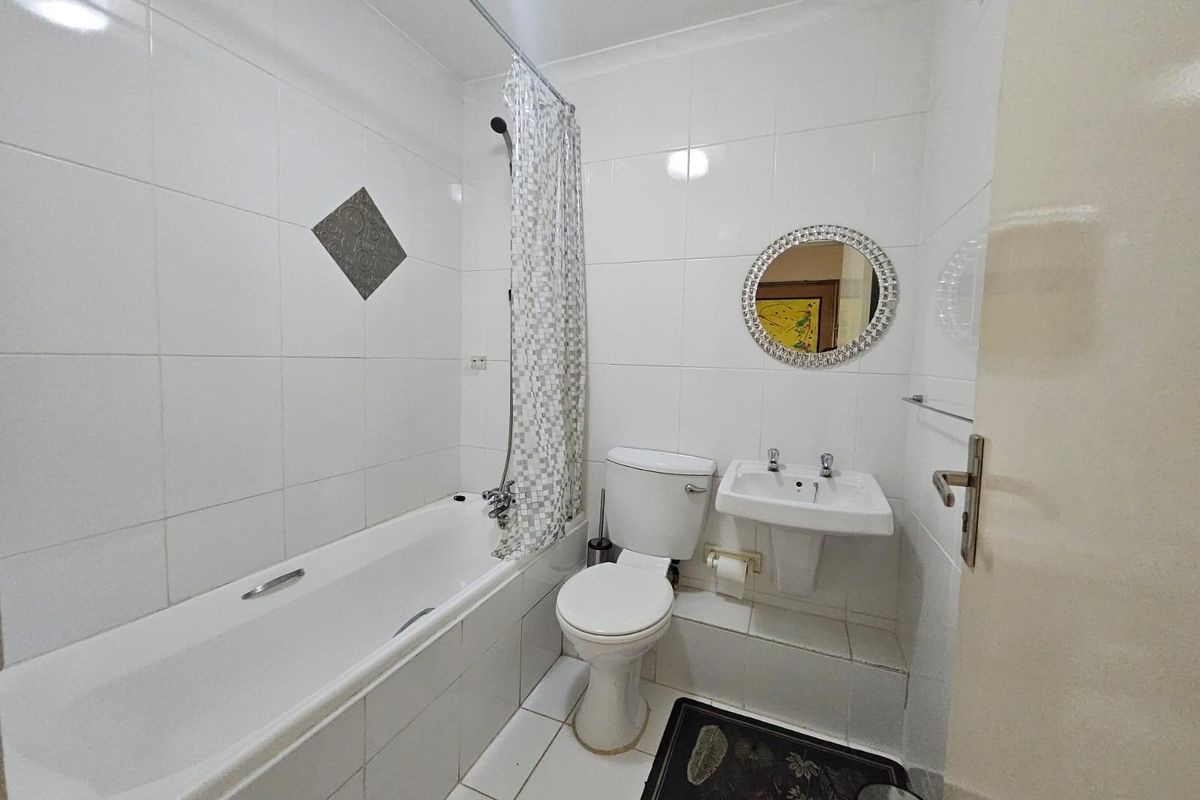 A functional bathroom featuring a bathtub with shower attachment, pedestal sink, and toilet, finished with white wall and floor tiles.
