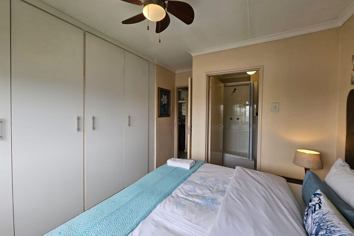 A bedroom featuring built-in cupboards, a ceiling fan, and an adjoining en-suite bathroom with a shower.
