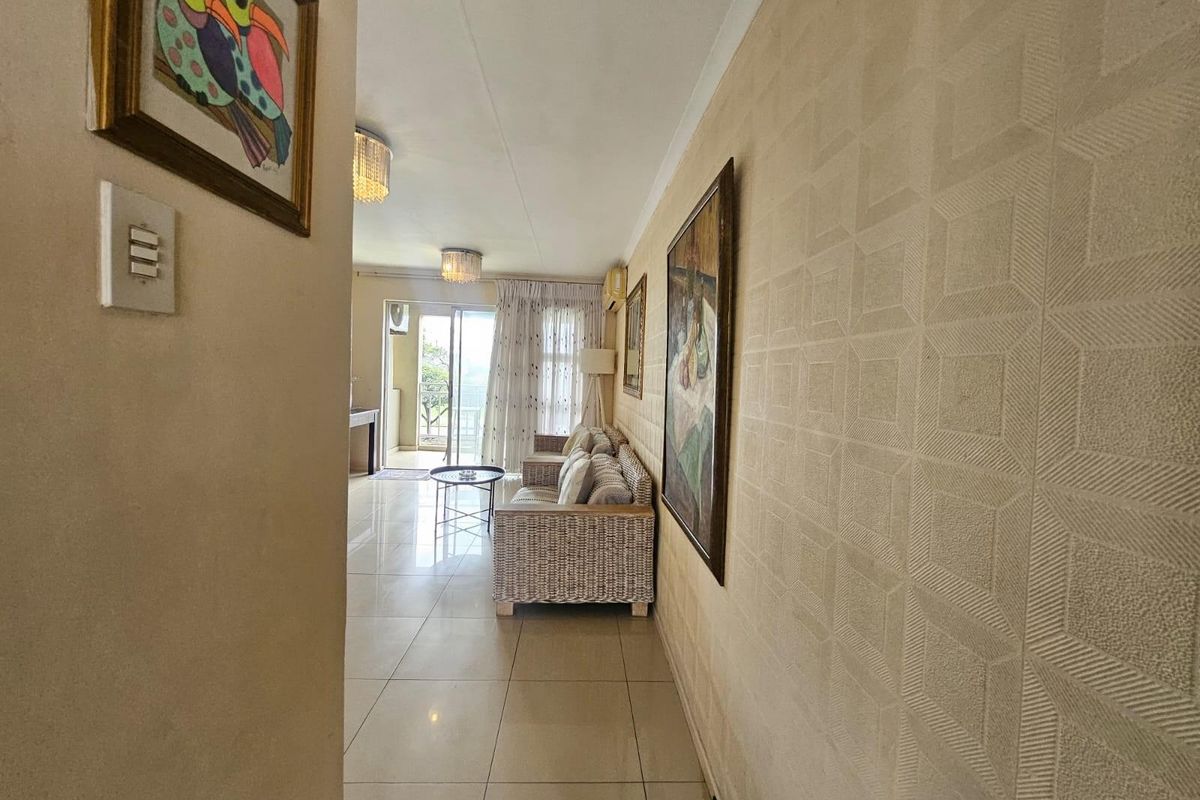 A bright living area featuring tiled floors, textured wallpaper, and direct access to a balcony through sliding glass doors.