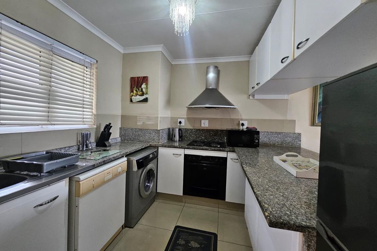 A functional kitchen featuring granite countertops, built-in cabinetry, a stainless steel extractor fan, and integrated oven and hob, with tiled flooring throughout.