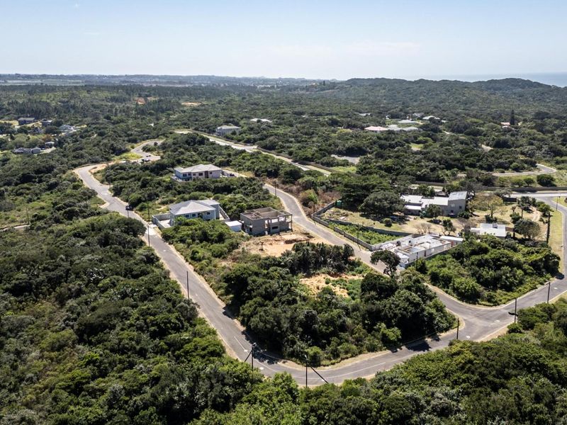 An aerial view of a residential estate featuring paved roads, established coastal vegetation, and surrounding residential plots.
