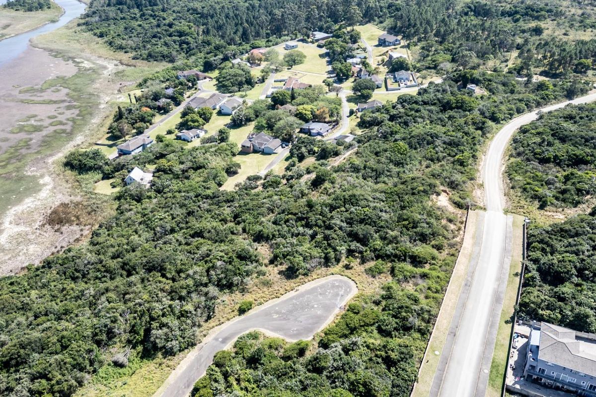 Aerial view of a vacant residential plot featuring natural coastal vegetation, road access, and proximity to the estuary.